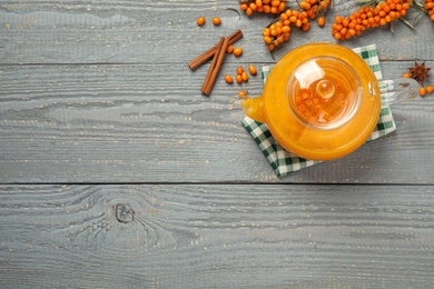 Delicious sea buckthorn tea, fresh berries and spices on grey wooden table, flat lay. Space for text