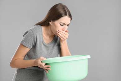 Woman with basin suffering from nausea on grey background. Food poisoning
