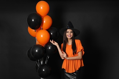 Photo of Beautiful woman wearing witch costume with balloons for Halloween party on black background