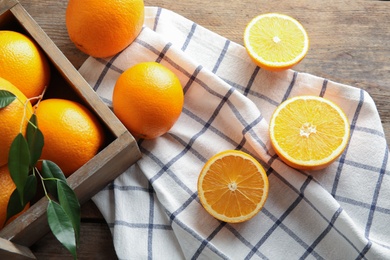 Fresh oranges with leaves and rustic box on wooden table, above view