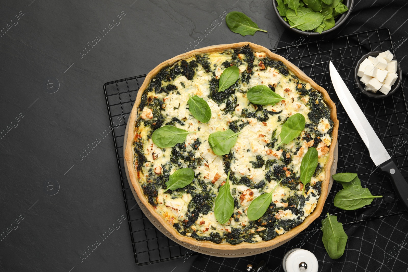 Photo of Delicious homemade spinach quiche and ingredients on black table, flat lay