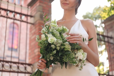 Photo of Gorgeous bride in beautiful wedding dress with bouquet near church, closeup