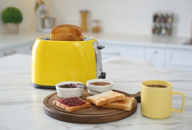 Modern toaster and tasty breakfast on white marble table in kitchen