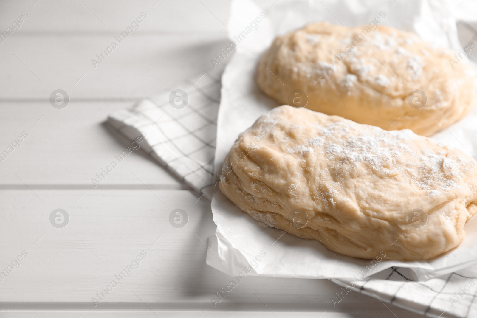 Photo of Raw dough and flour on white wooden table, space for text. Cooking ciabatta