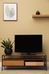 Photo of Modern TV on cabinet and green plants near beige wall in room. Interior design