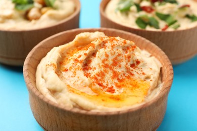 Photo of Bowl of tasty hummus with paprika on blue background, closeup