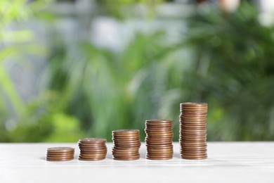 Photo of Stacked coins on white table against blurred green background. Space for text