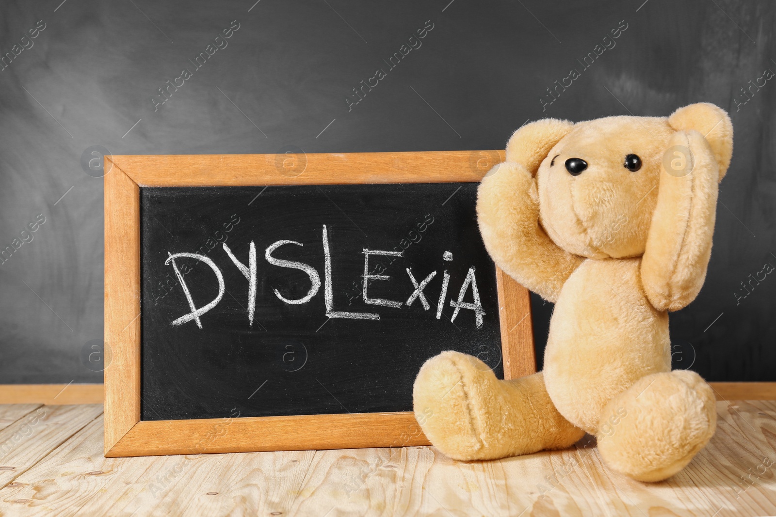 Photo of Teddy bear and small blackboard with word Dyslexia on wooden table