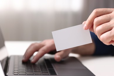 Photo of Man with laptop holding blank business card at white table indoors, closeup