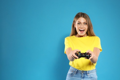 Emotional young woman playing video games with controller on color background. Space for text