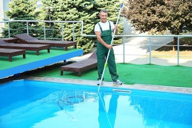 Photo of Male worker cleaning outdoor pool with underwater vacuum