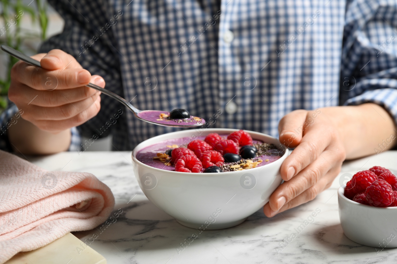 Photo of Woman eating tasty acai smoothie with fruits at white marble table, closeup