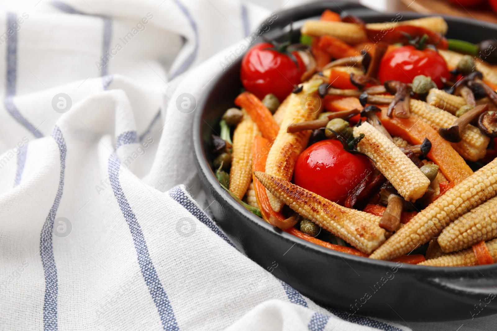 Photo of Tasty roasted baby corn with tomatoes, capers and mushrooms on table, closeup