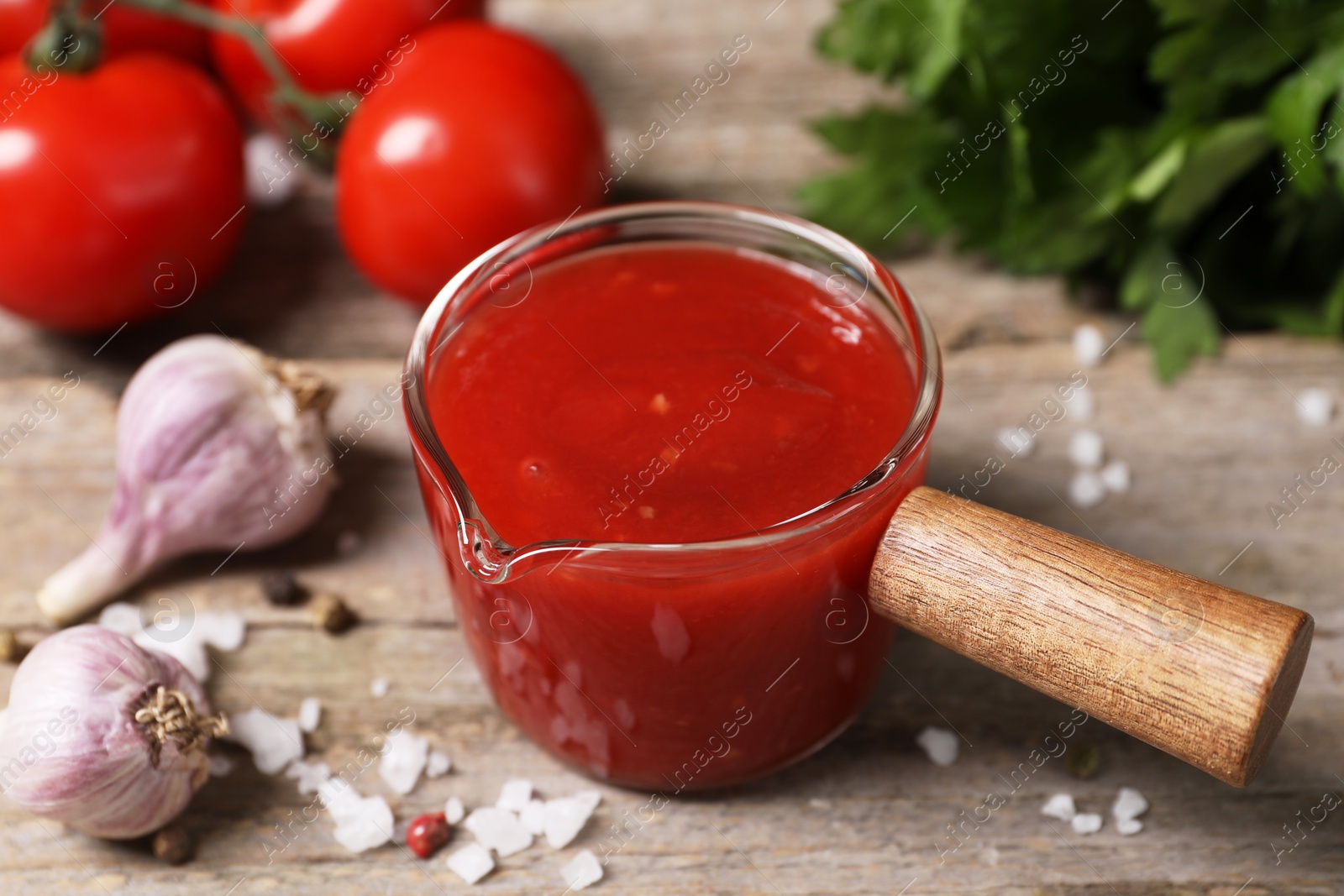 Photo of Delicious ketchup, salt and garlic on wooden table, closeup. Tomato sauce