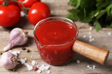 Photo of Delicious ketchup, salt and garlic on wooden table, closeup. Tomato sauce