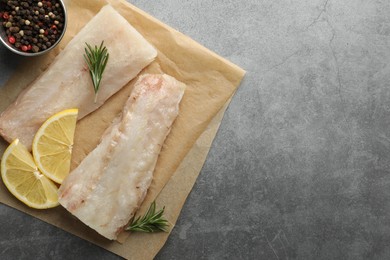 Photo of Fresh raw cod fillets, spices and lemon slices on grey table, flat lay. Space for text