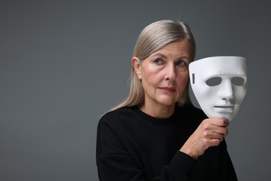 Photo of Multiple personality concept. Woman with mask on gray background, space for text