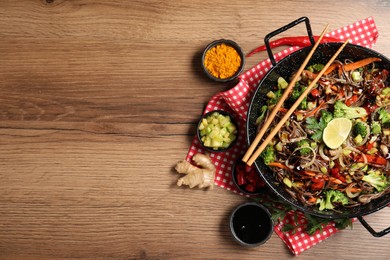 Photo of Stir-fry. Tasty noodles with meat in wok, chopsticks and ingredients on wooden table, flat lay. Space for text