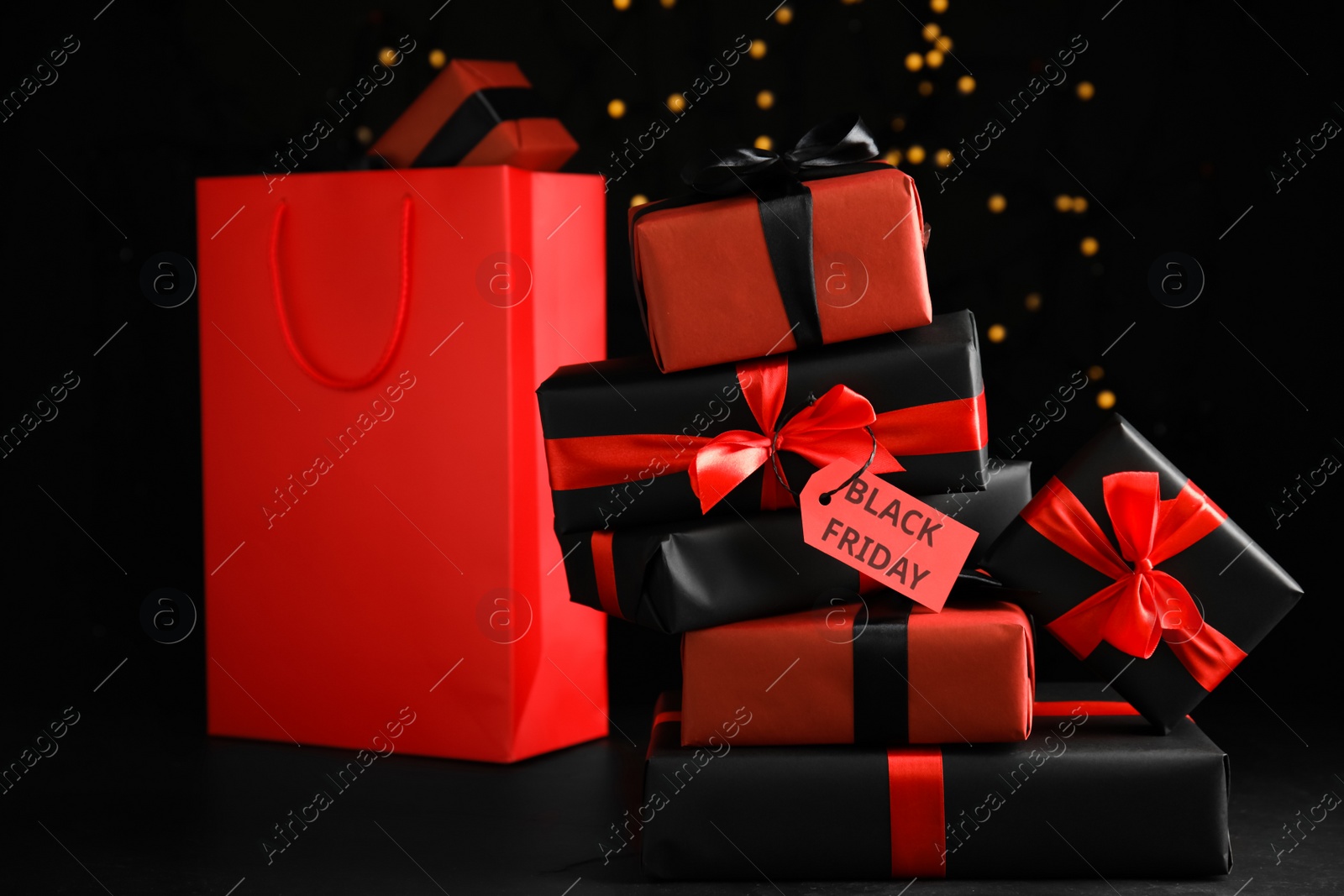 Photo of Gift boxes with Black Friday tag and shopping bag against blurred lights