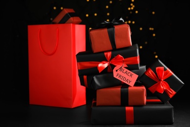 Gift boxes with Black Friday tag and shopping bag against blurred lights
