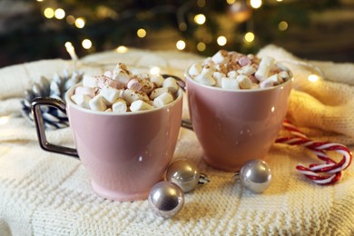 Cups of tasty cocoa with marshmallows, candy canes and Christmas decor on knitted plaid indoors