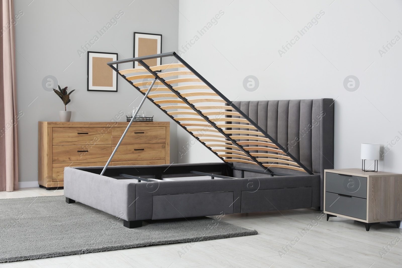 Photo of Comfortable bed with storage space for bedding under lifted slatted base in stylish room