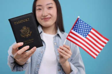 Photo of Immigration to United States of America. Woman with passport and flag on light blue background, selective focus