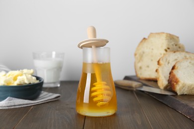 Photo of Jar of tasty honey, milk, butter and bread on wooden table