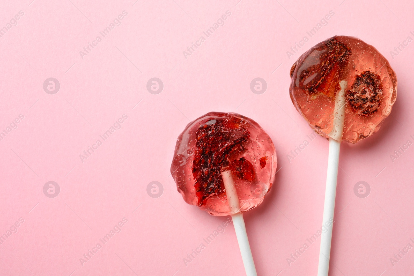 Photo of Sweet colorful lollipops with berries on pink background, flat lay. Space for text