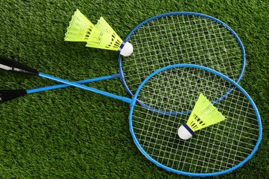 Photo of Badminton rackets and shuttlecocks on green grass outdoors, flat lay