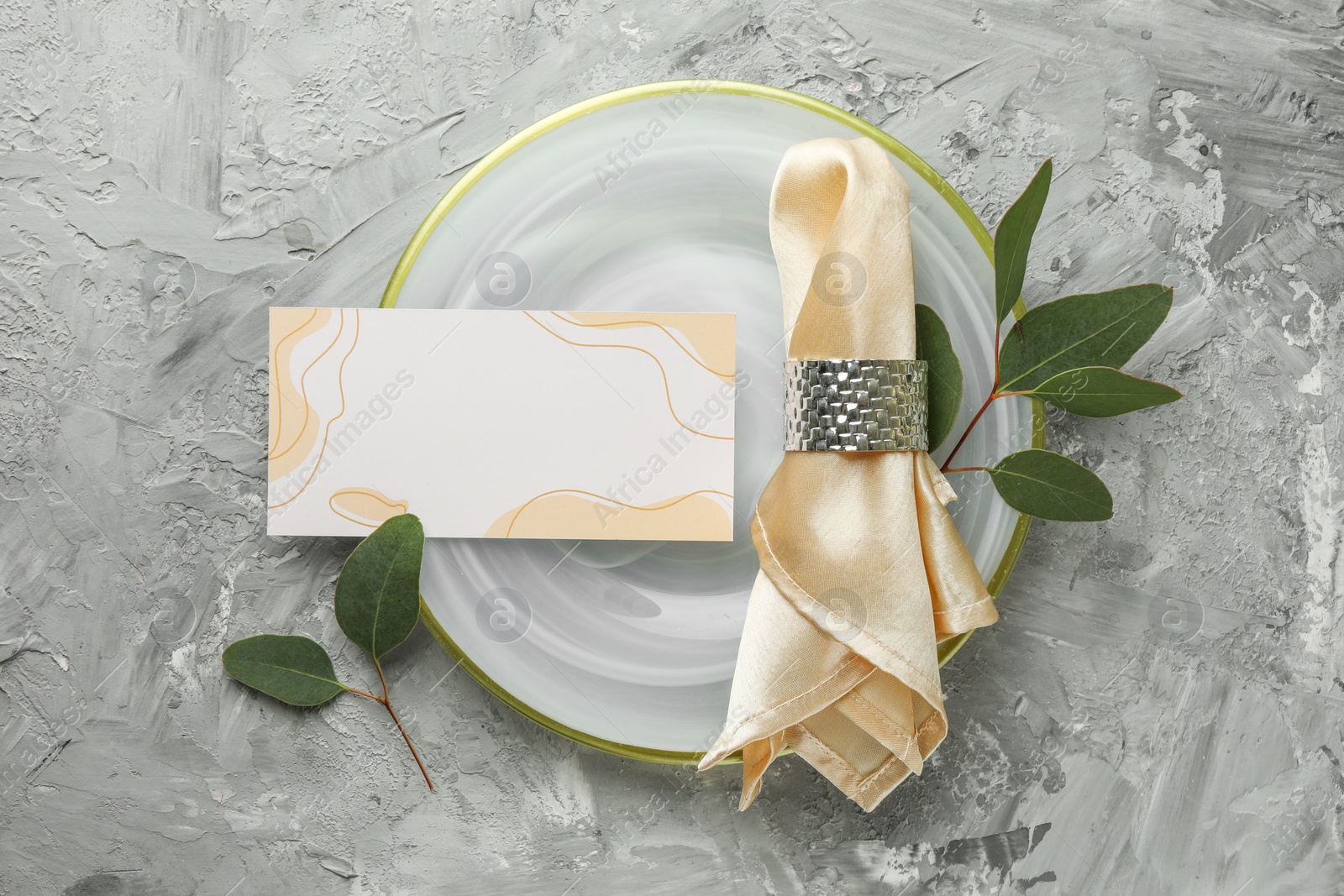 Photo of Blank invitation card, plate, napkin and eucalyptus leaves on grey table, flat lay. Space for text