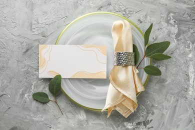 Photo of Blank invitation card, plate, napkin and eucalyptus leaves on grey table, flat lay. Space for text