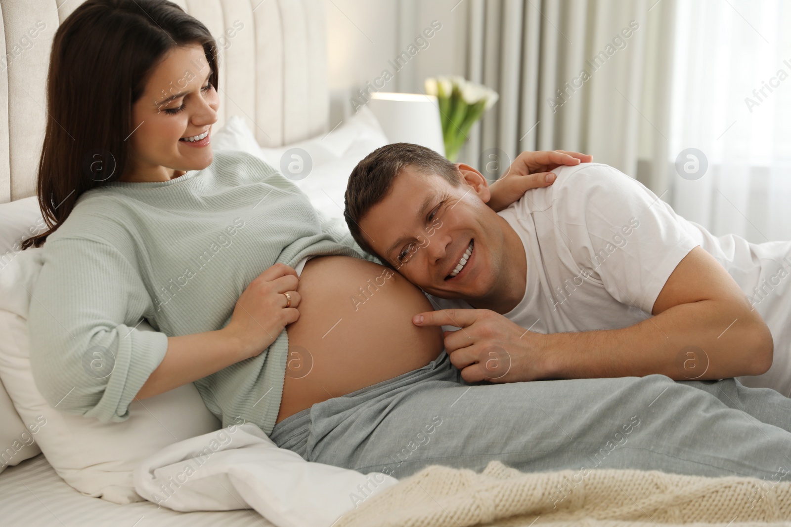 Photo of Young pregnant woman with her husband in bedroom