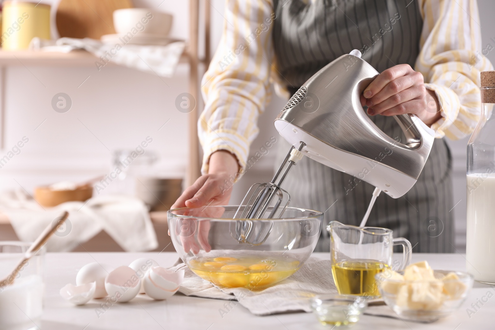 Photo of Woman making dough with mixer in bowl at table, closeup