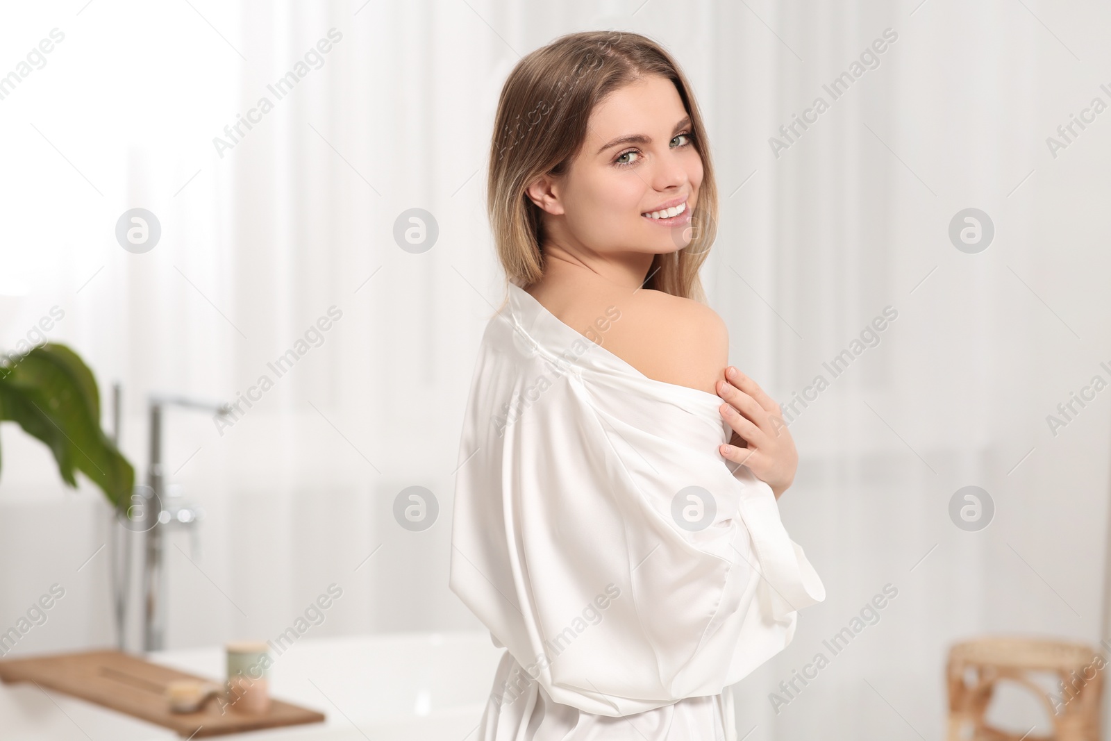 Photo of Beautiful happy woman wearing stylish white robe in light bathroom