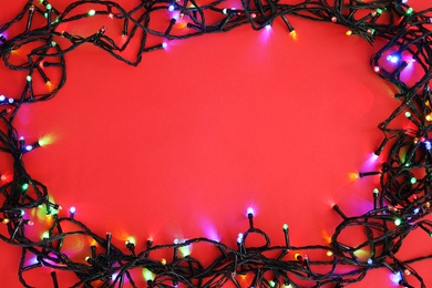 Glowing Christmas lights on color background, top view