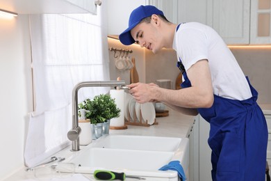 Photo of Smiling plumber repairing faucet with spanner in kitchen