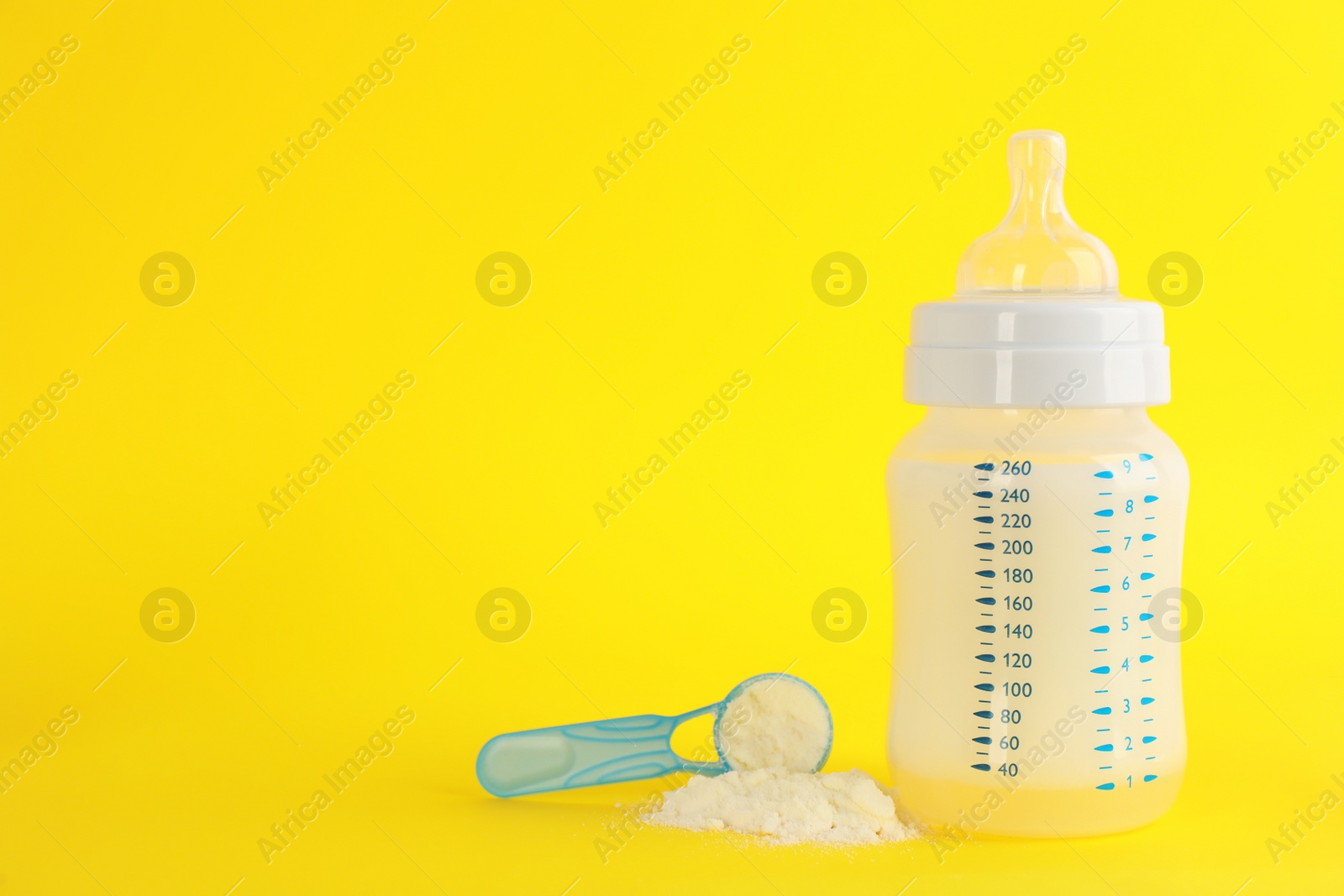 Photo of Feeding bottle with infant formula and scoop of powder on yellow background, space for text. Baby milk