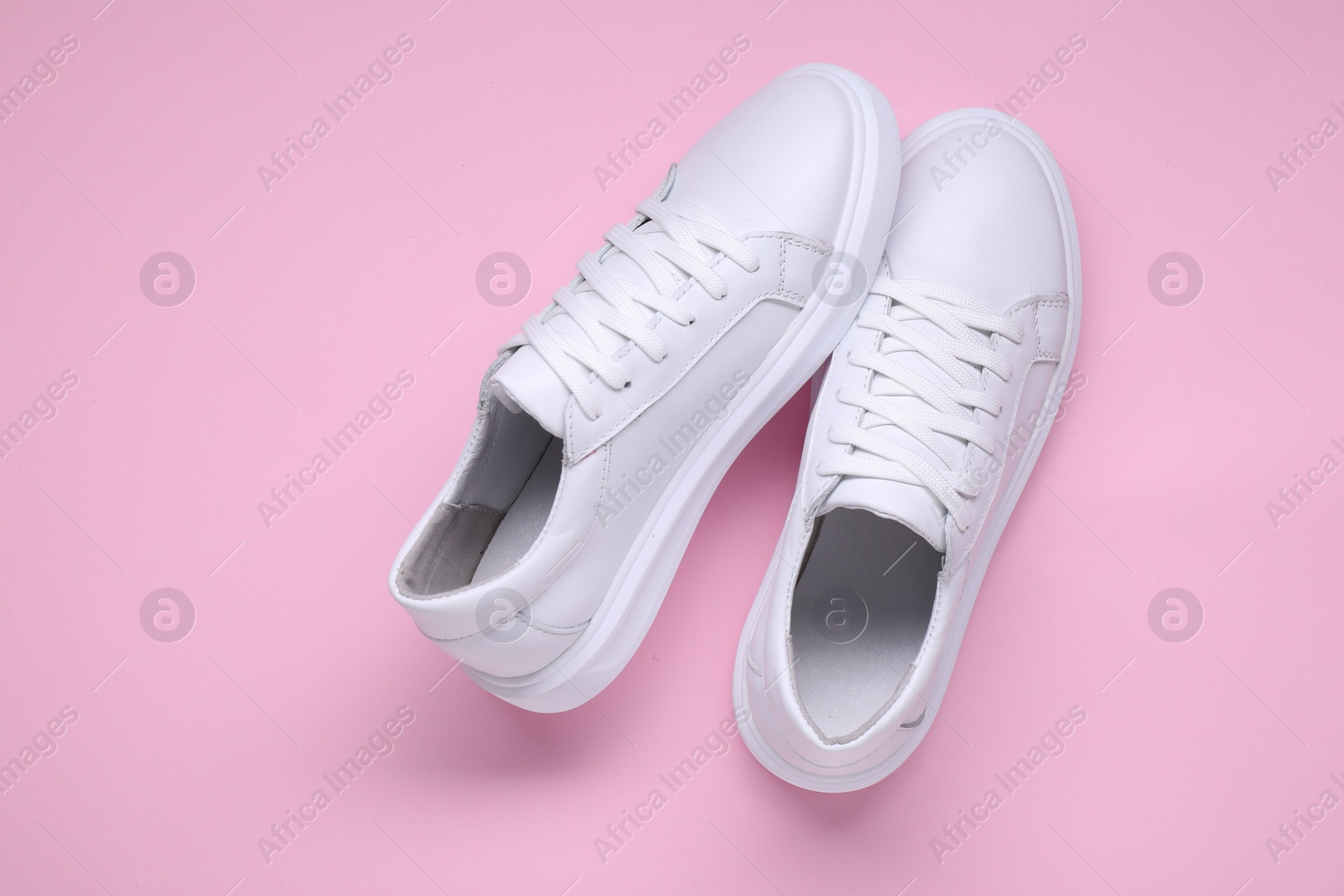 Photo of Pair of stylish white sneakers on pink background, top view