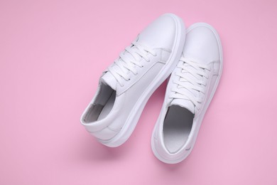 Pair of stylish white sneakers on pink background, top view