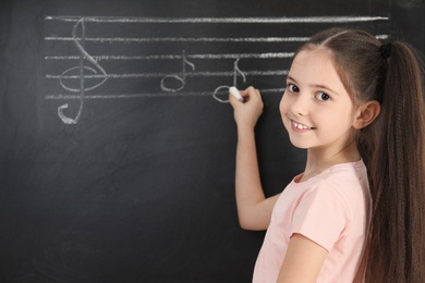 Photo of Little girl writing music notes on blackboard. Space for text