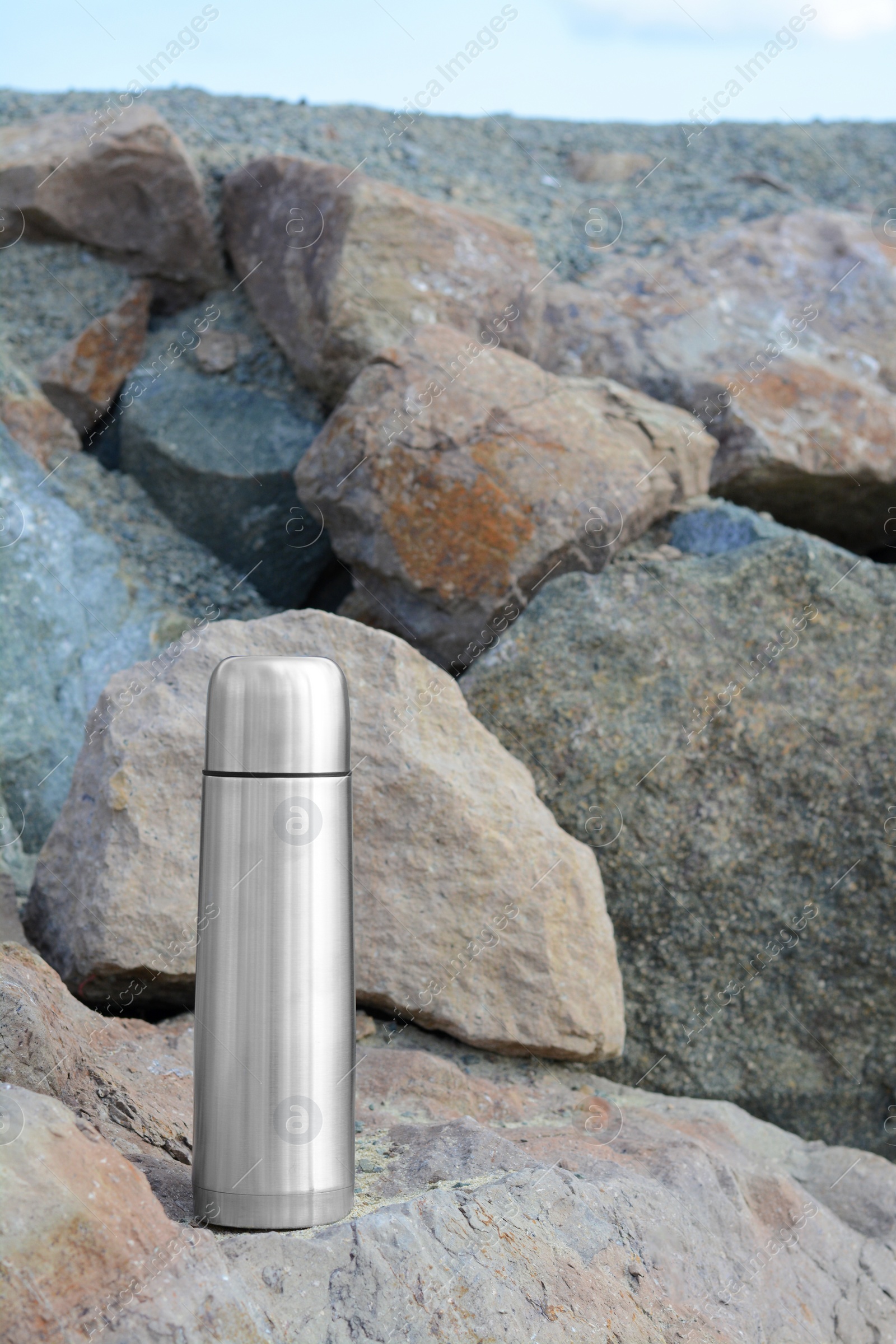 Photo of Metallic thermos with hot drink on stone outdoors, space for text