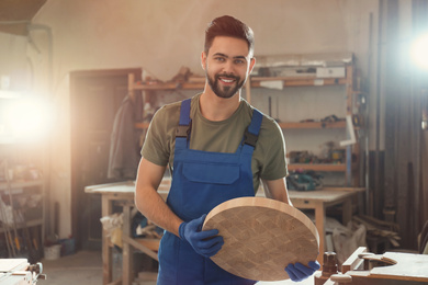 Photo of Professional carpenter with round piece of wood in workshop