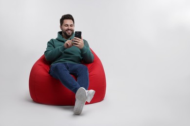 Happy young man using smartphone on bean bag chair against white background, space for text