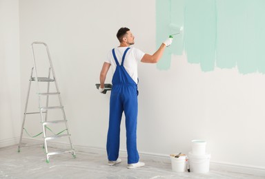 Image of Man painting wall with light blue dye indoors