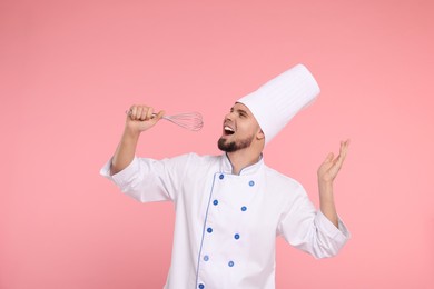 Happy professional confectioner in uniform having fun with whisk on pink background