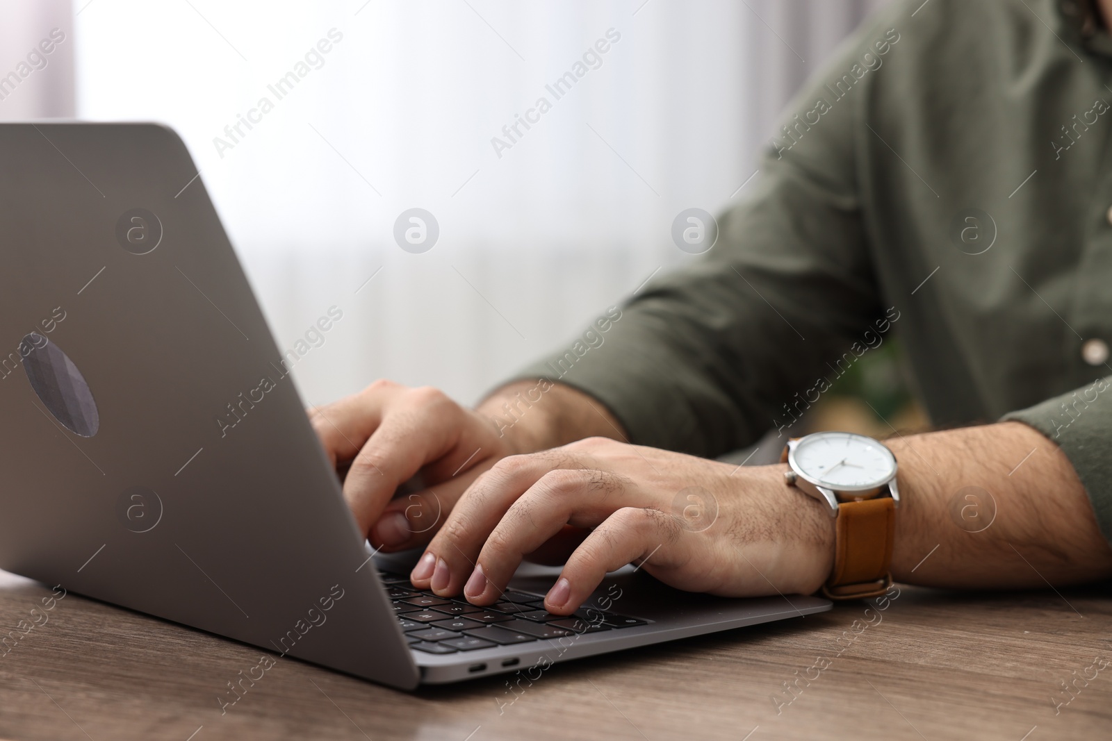 Photo of E-learning. Young man using laptop at wooden table indoors, closeup