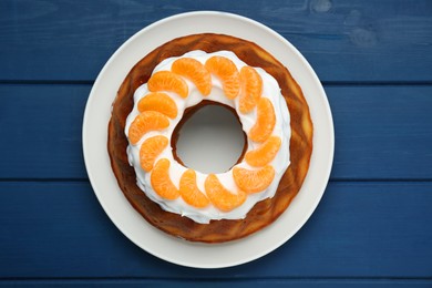 Photo of Homemade yogurt cake with tangerines and cream on blue wooden table, top view