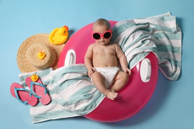 Cute little baby in sunglasses with inflatable ring and beach accessories on light blue background, top view