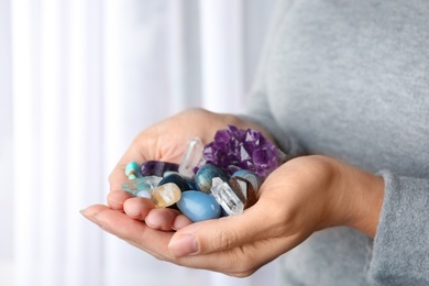 Photo of Woman holding pile of different gemstones indoors, closeup